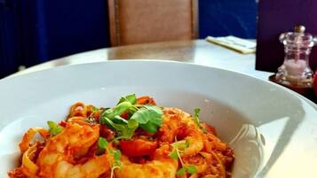 Un piatto di pasta con frutti di mare su un piatto bianco, con un menu e un logo sul tavolo.