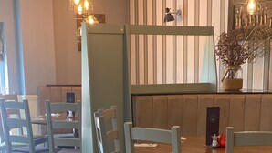 Een restaurant met houten tafels en stoelen, een balie en hangende lampen.
