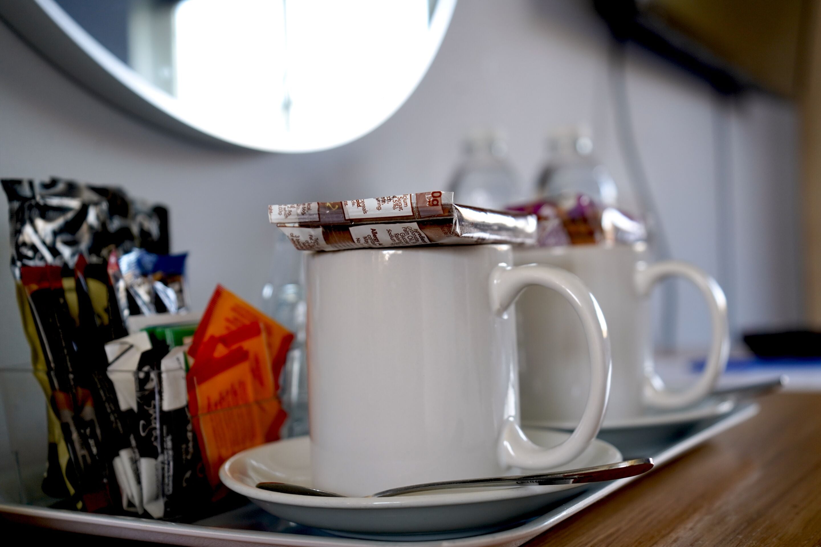 Une table avec deux tasses et sous-tasses blanches, une cuillère et des sachets de café instantané.