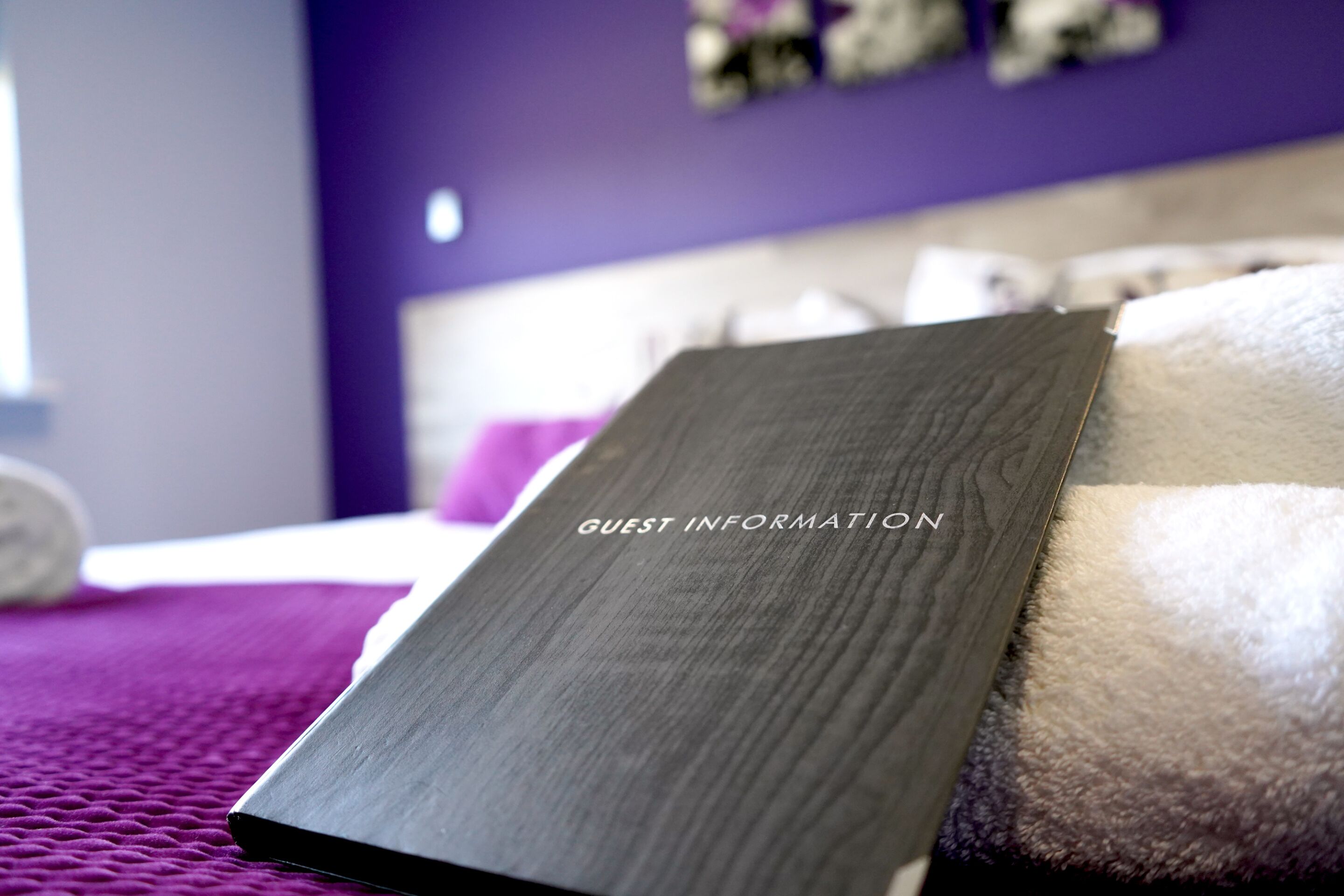 A room with a bed, a purple wall, and a sign labeled "GUEST INFORMATION".