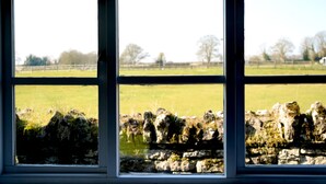 Een raam met uitzicht op een stenen muur en een grasveld.