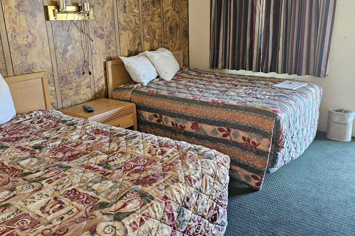 A hotel room with two beds, a wooden headboard, a striped curtain, and a small trash bin.