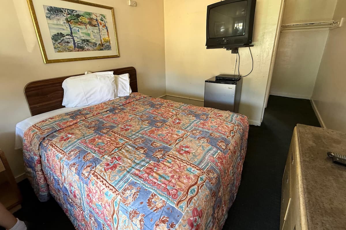 A hotel room with a bed, a television, a small desk, and a painting on the wall.