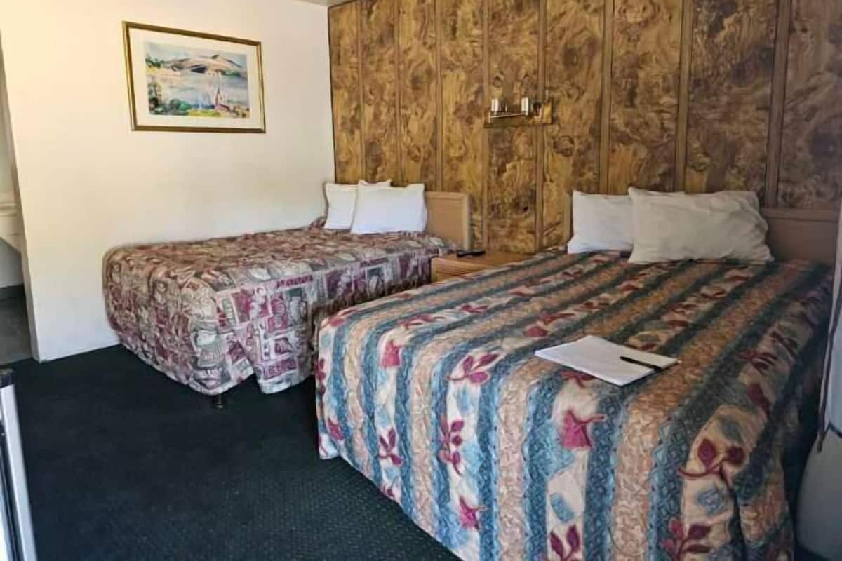A room with two beds, a wooden headboard, a painting on the wall, and a desk.