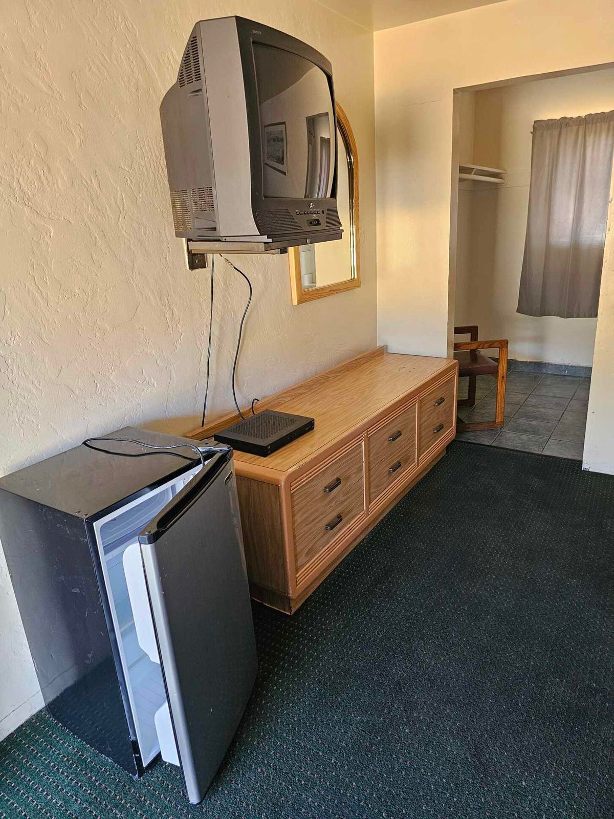 A compact room with a wooden desk, a black refrigerator, and a mounted television.