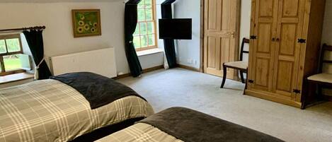 A bedroom with two beds, a wooden wardrobe, a chair, and a window with curtains.