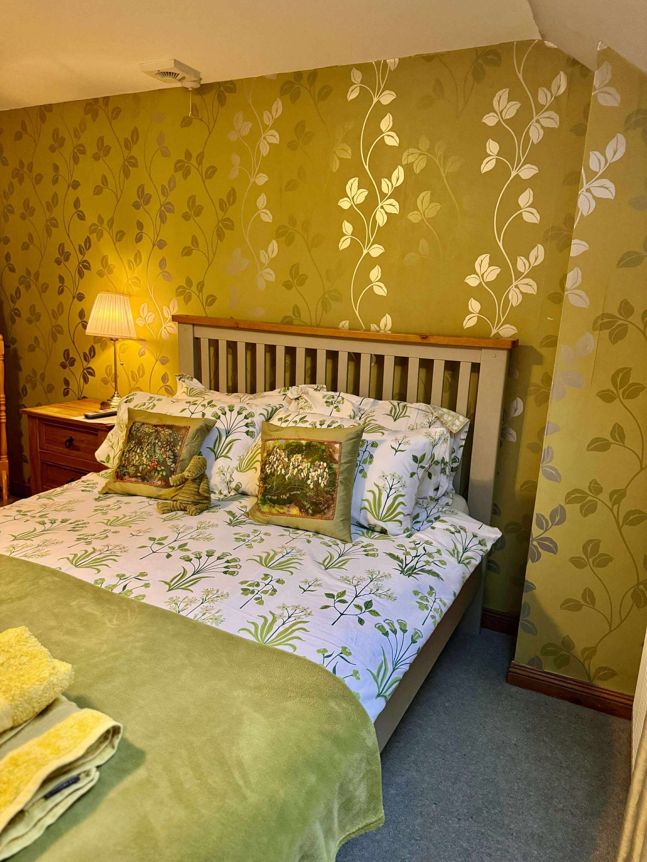 A neatly made bed with floral bedding, a wooden headboard, and a bedside lamp.