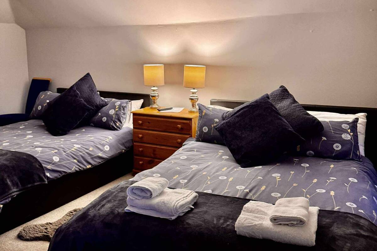 A hotel room with two single beds, a wooden nightstand with two lamps, and a ceiling light fixture.