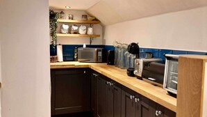 A modern kitchen with dark cabinets, a wooden countertop, and a microwave. - Lodge at Lochside (Kirriemuir)
