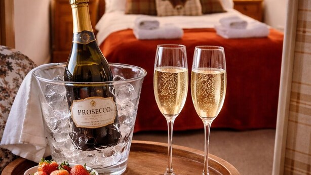 A bottle of Prosecco, two glasses of champagne, and a bowl of strawberries on a wooden tray in a hotel room. - Lodge at Lochside (Kirriemuir)