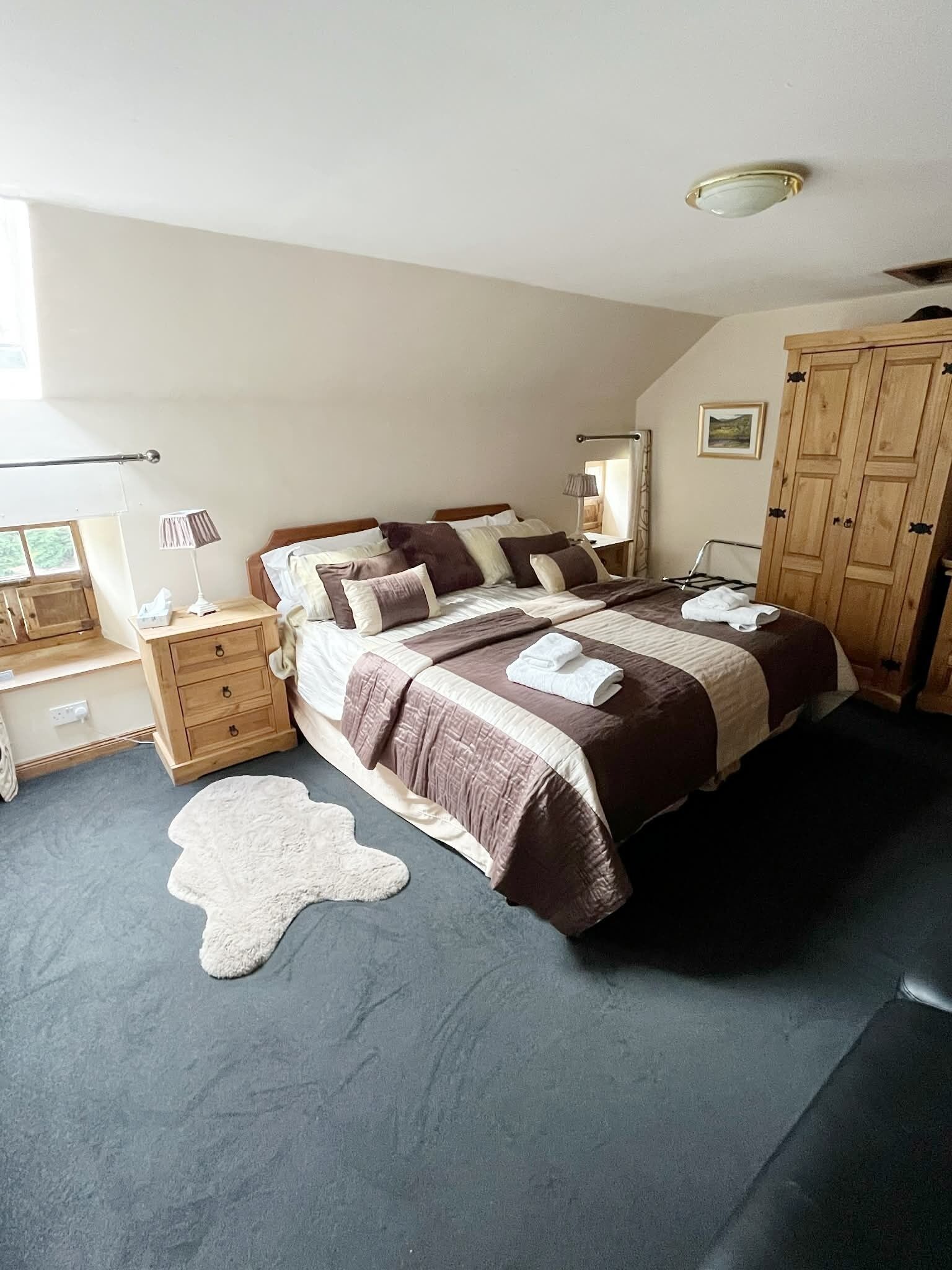 A bedroom with a large bed, wooden wardrobe, bedside tables, a lamp, and a rug.