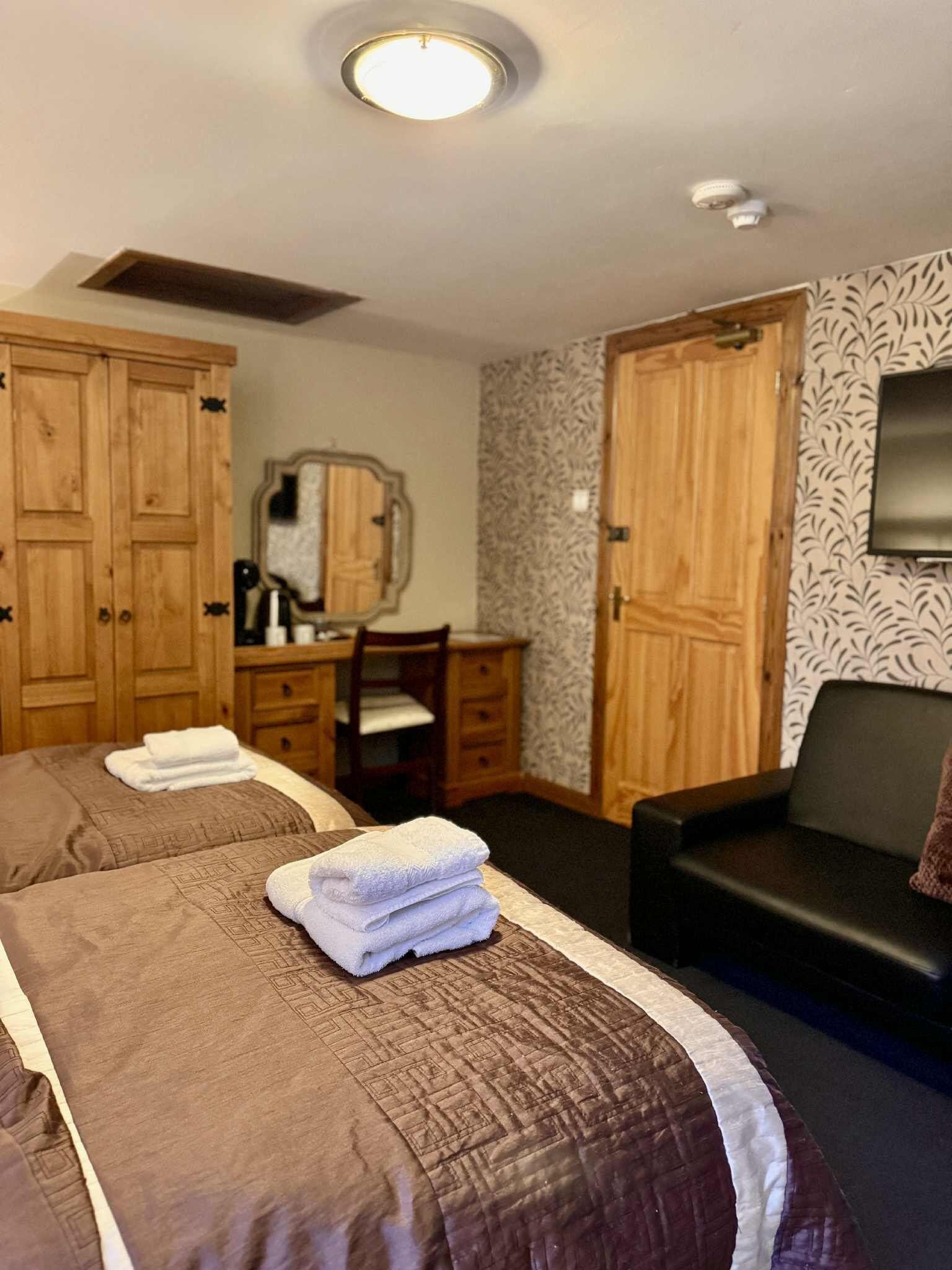 A hotel room with two beds, a desk, a mirror, a TV, and a sofa.
