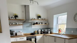 A modern kitchen with wooden countertops, white cabinets, and a built-in oven. There are two stools and a window with a view of the outside. - Lodge at Lochside (Kirriemuir)