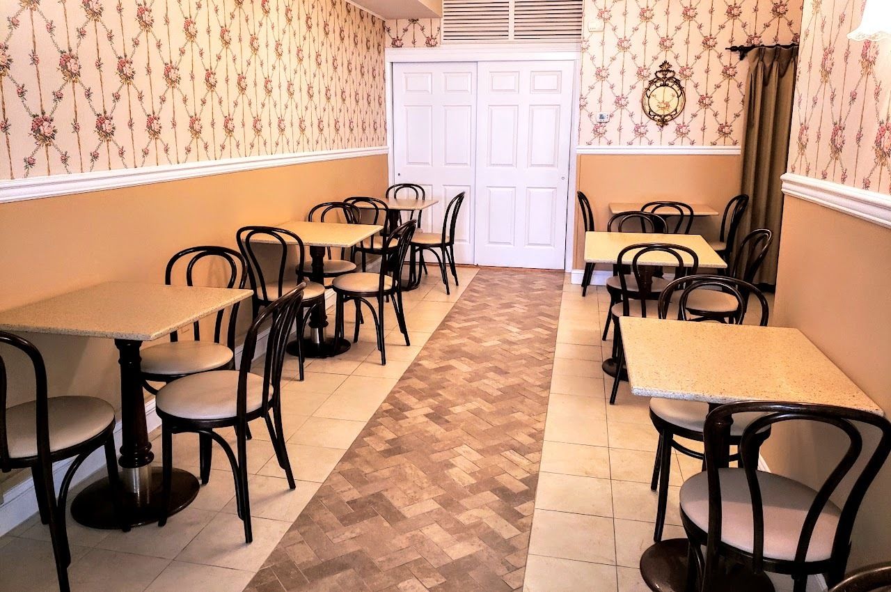 Uma área de refeições com várias mesas e cadeiras, papel de parede estampado e piso em padrão herringbone.