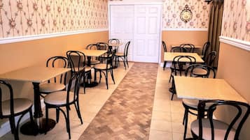 Un comedor con varias mesas y sillas, un papel tapiz estampado y un suelo de espiga.