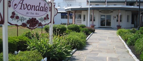 A sign for Avondale by the sea, a white building with a balcony, and a stone pathway.
