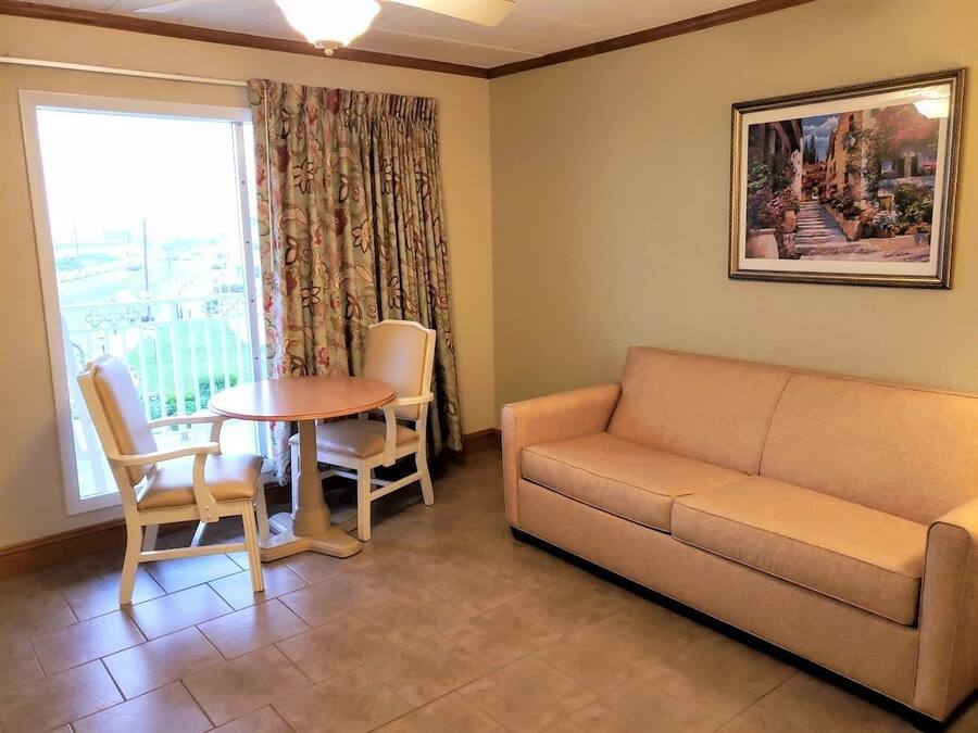 A living room with a beige sofa, a wooden dining table with two chairs, and a large window with floral curtains.