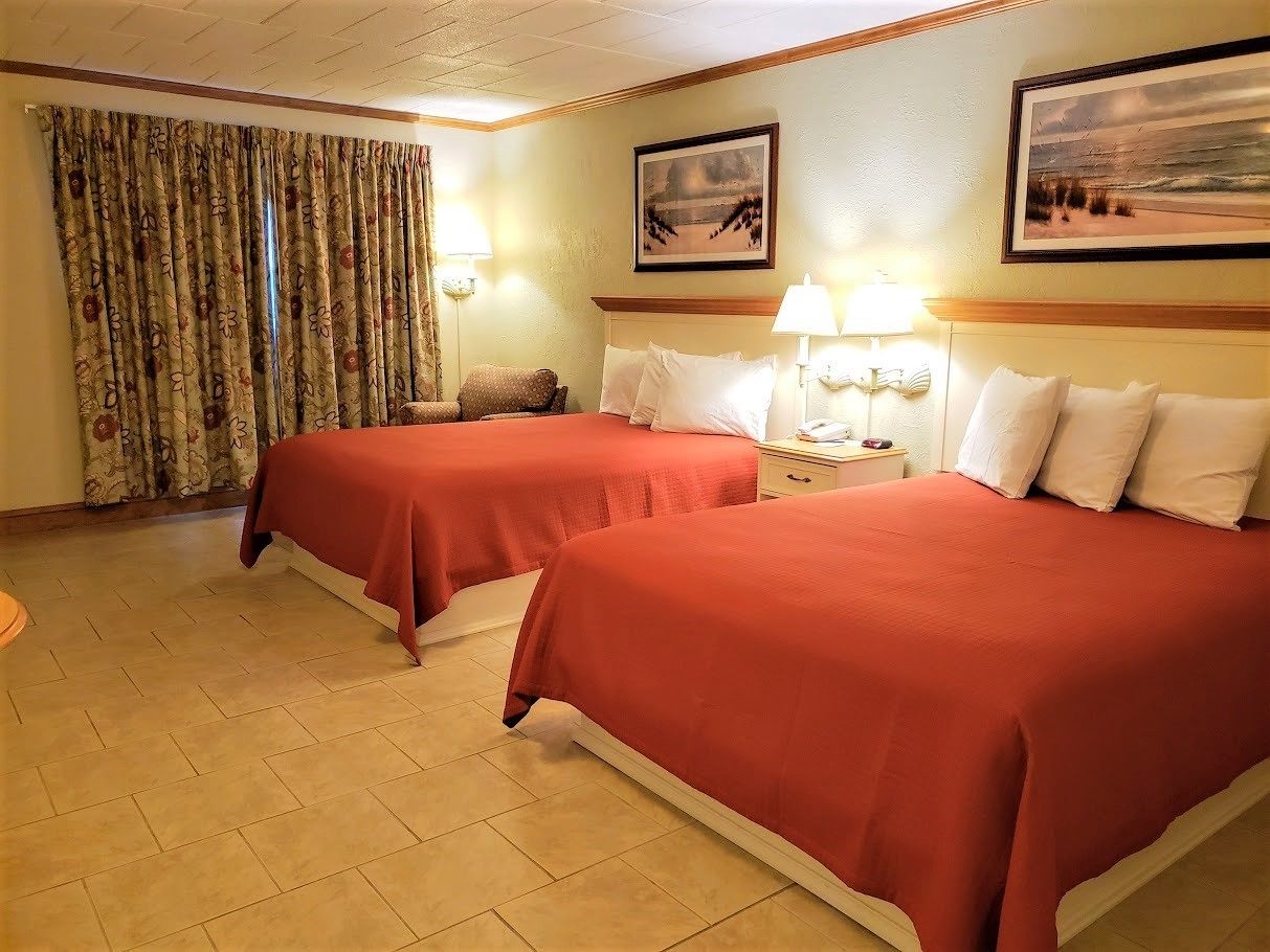 Une chambre d’hôtel avec deux lits, une grande fenêtre avec des rideaux et un tableau au mur.