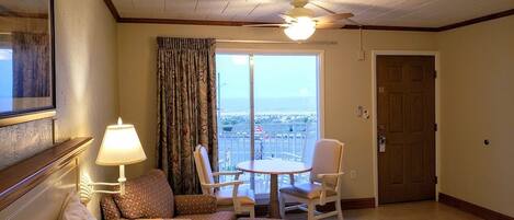 Een hotelkamer met een bed, een zithoek met een tafel en stoelen, een raam met gordijnen en een deur.