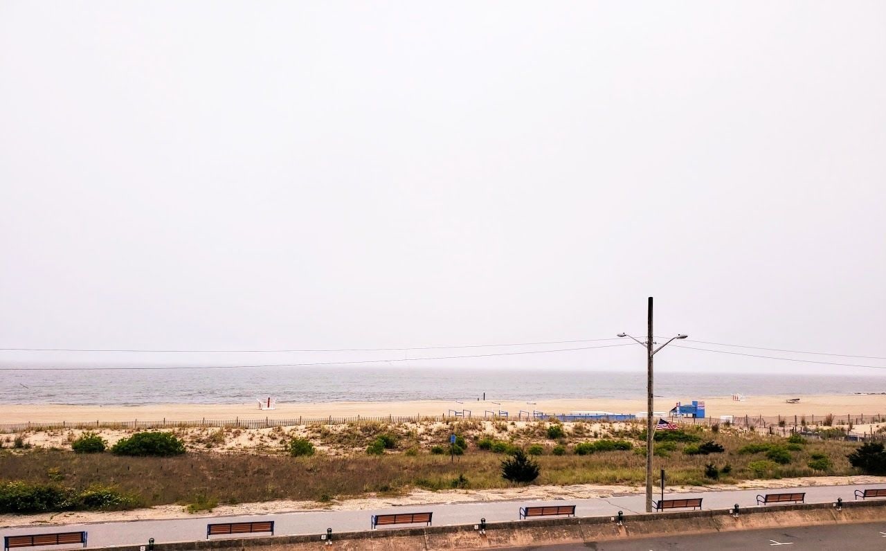 Une vue sur la plage avec une route, des bancs et une clôture.