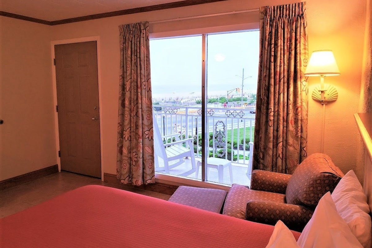 Une chambre d’hôtel avec un grand lit, un balcon donnant sur la ville et un fauteuil.