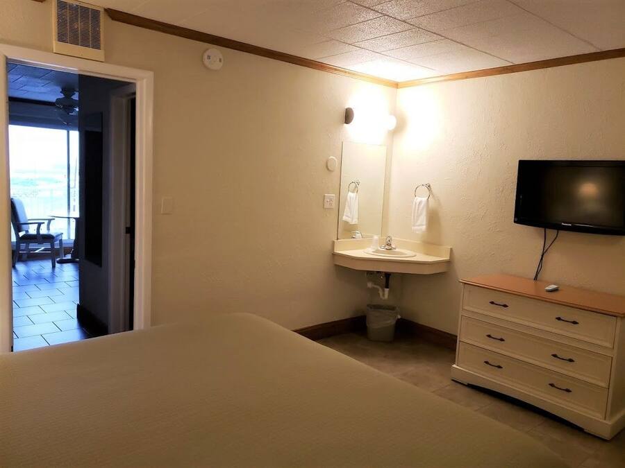 A hotel room with a bed, a sink, a mirror, a television, and a view of the outside balcony.