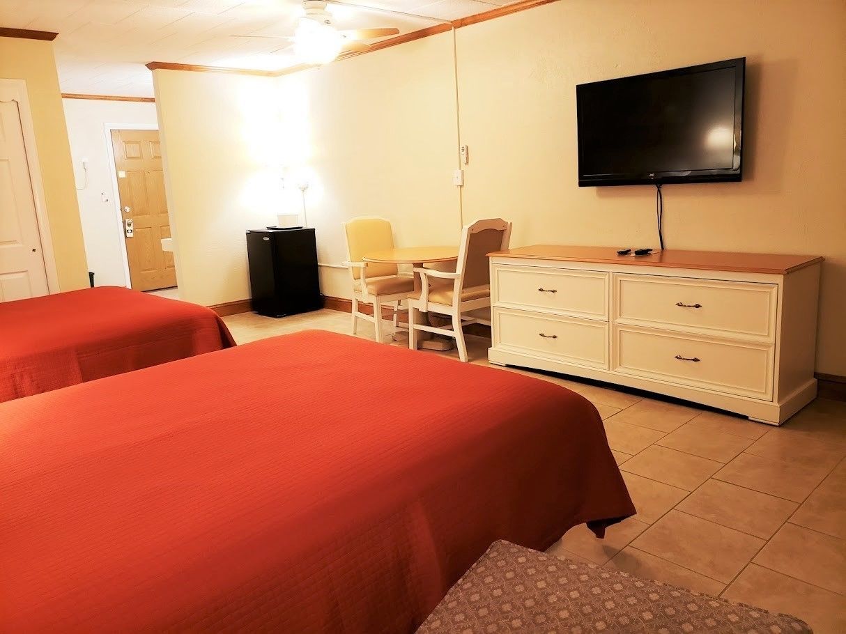 A hotel room with two beds, a desk, a chair, a TV, and a dresser.