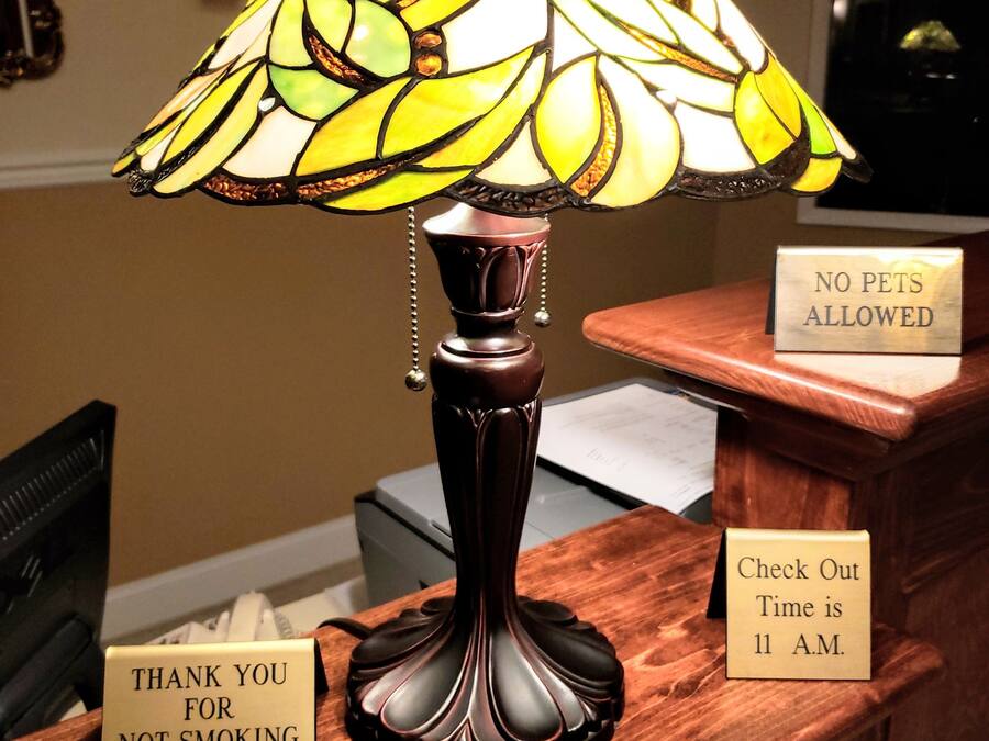 A lobby area with a stained glass lamp, a 'No Pets Allowed' sign, a 'Thank You for Not Smoking' sign, and a 'Check Out Time is 11 A.M.' sign.