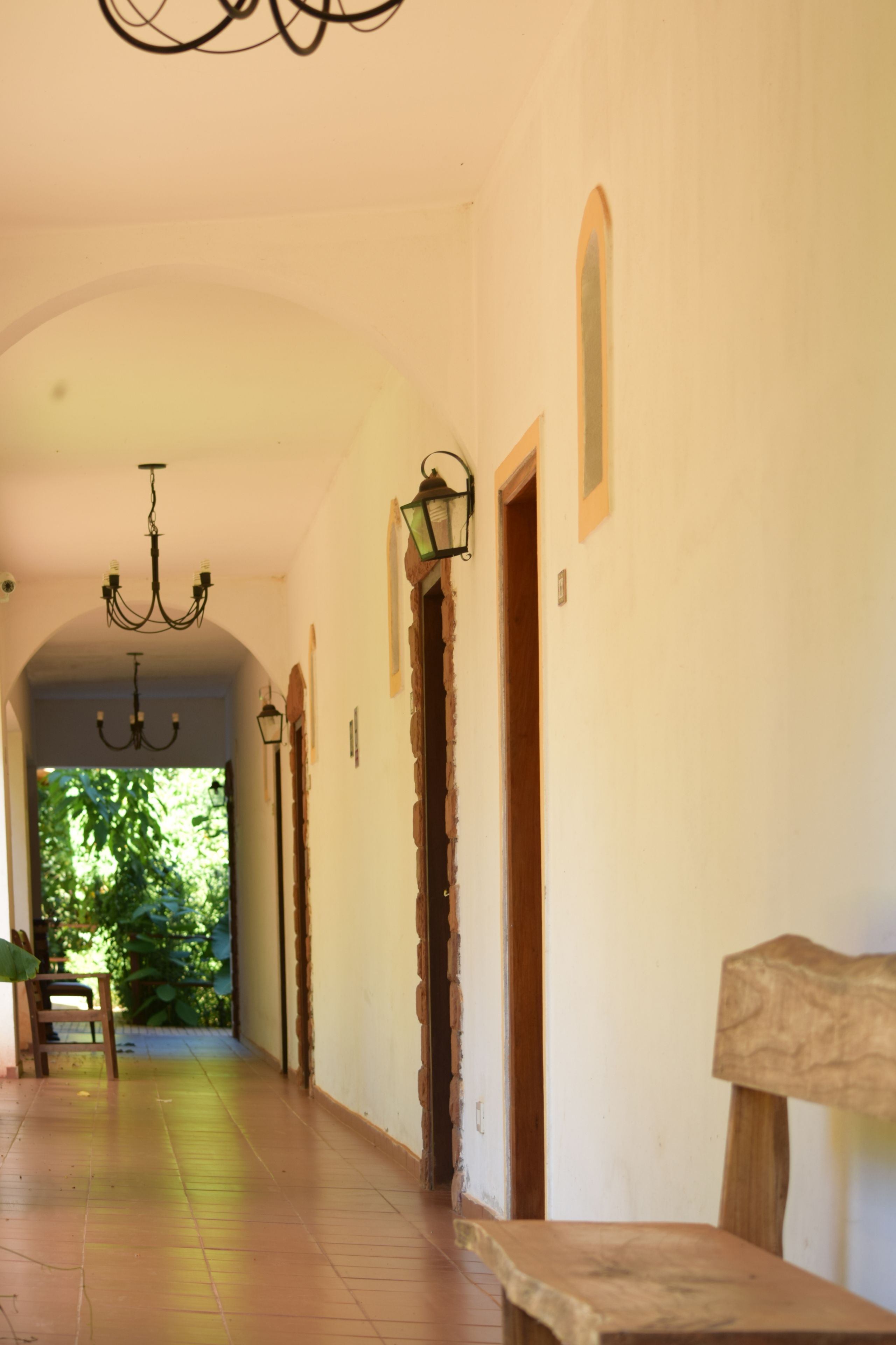 A corridor with a chandelier, wooden doors, and a bench.