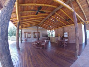 A covered outdoor area with wooden flooring, tables, chairs, and a stone wall. - El Pueblito Iguazu (Puerto Iguazú)