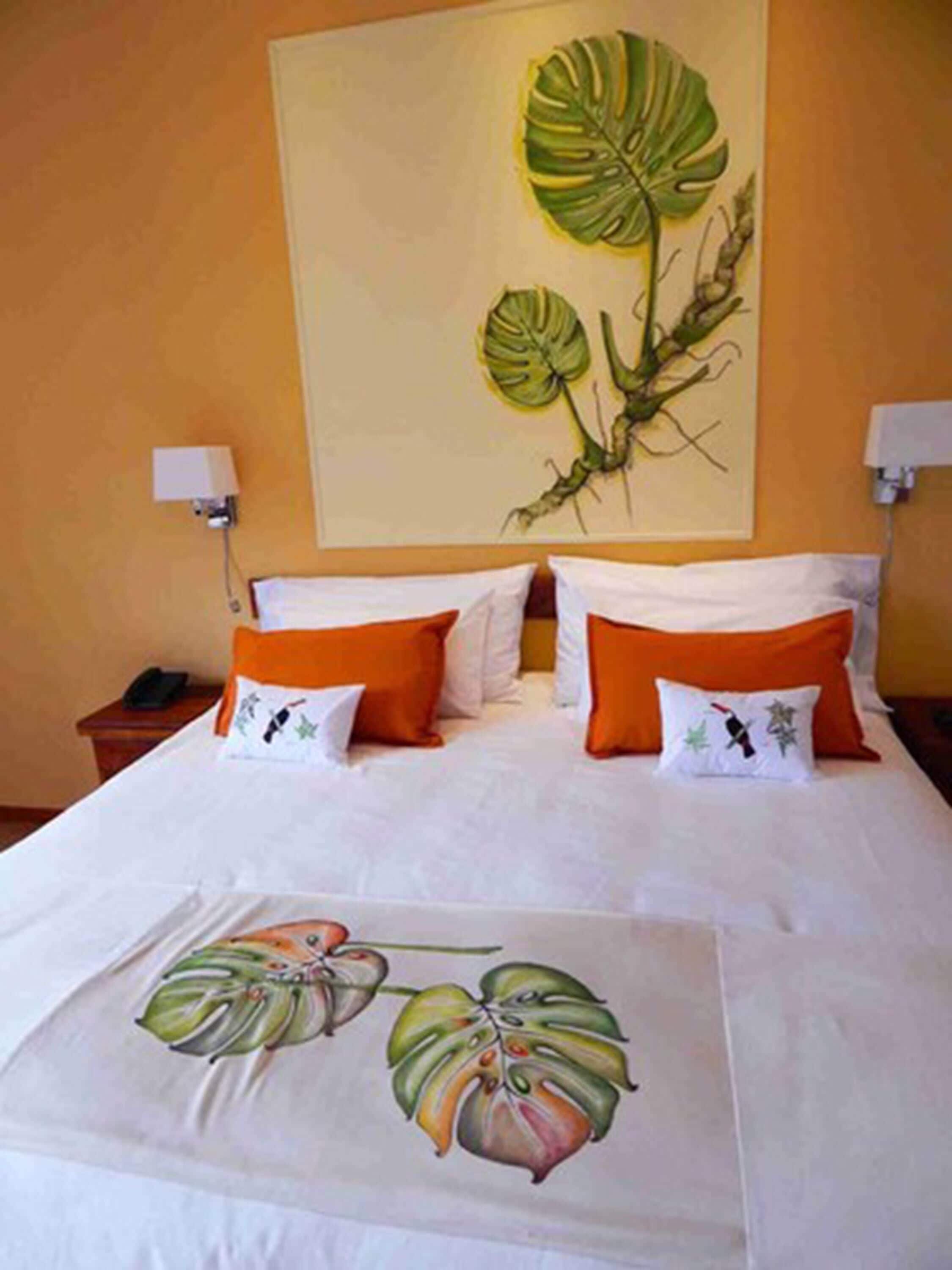 Een hotelkamer met een groot bed, twee bedlampjes en een wanddecoratie van een plant.