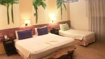 Habitación de hotel con dos camas, un banco de madera, una mesita de noche y una pared con murales de palmeras.
