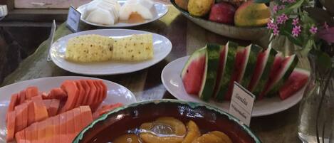 A table with various fruits and a bowl of sliced peaches.