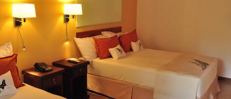 A hotel room with two beds, a nightstand with a phone, and wall-mounted lamps.