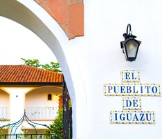A white building with a sign reading "EL PUEBLO DE IGUAZU" and a black lantern above it.