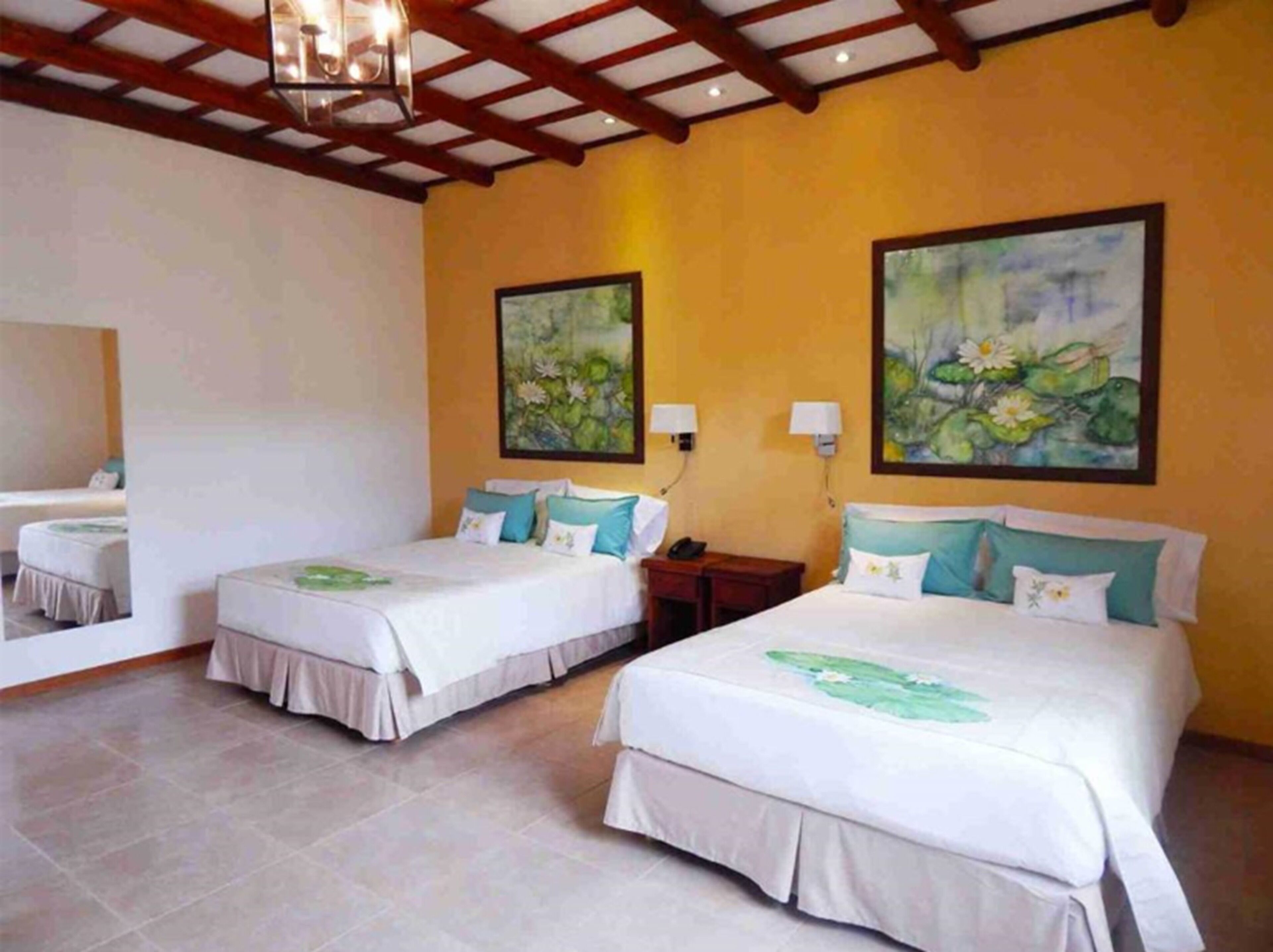 A hotel room with two beds, a wooden ceiling, and two paintings of water lilies on the walls.