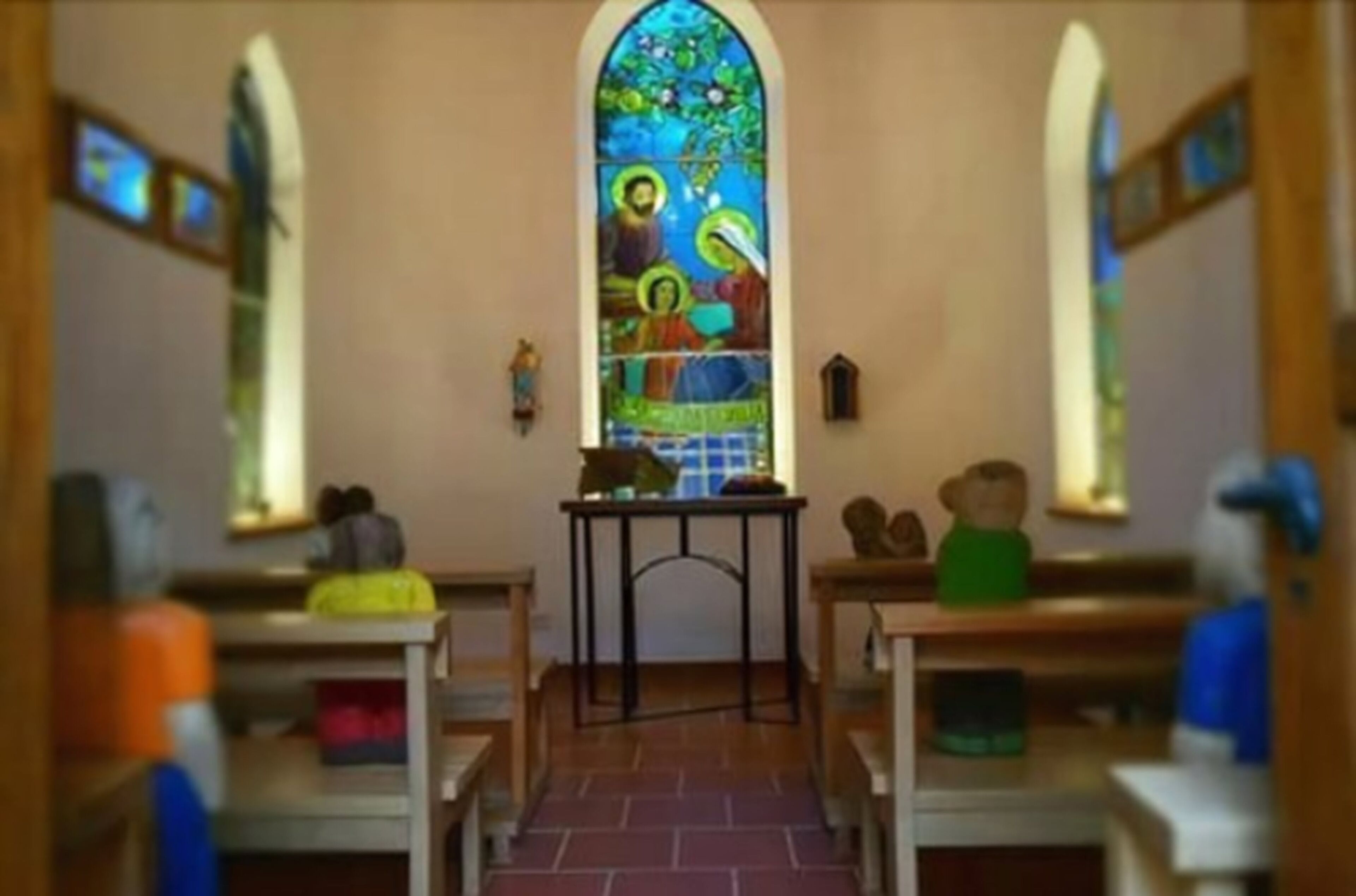 L’intérieur d’une église avec des bancs, un vitrail et une petite table d’autel.