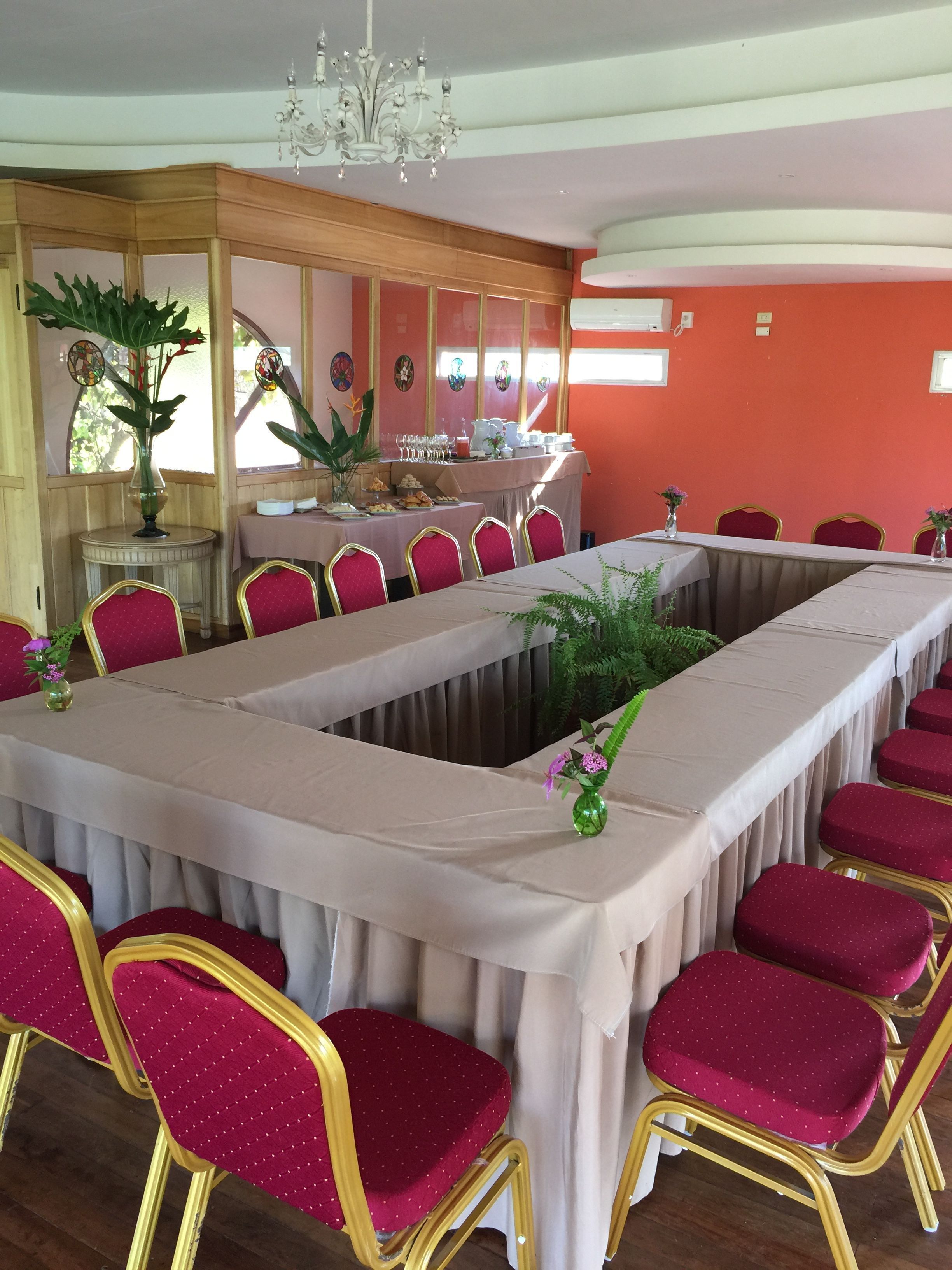 Un salón de conferencias con una larga mesa, sillas tapizadas en rojo y una lámpara de araña.
