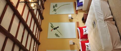 Una habitación con escalera de madera, cama con cubrecama blanco y tres obras de arte en la pared que representan paisajes naturales.