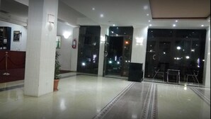 Una hall d'albergo con reception, una pianta in vaso, un estintore e una porta vetrata che dà all'esterno.