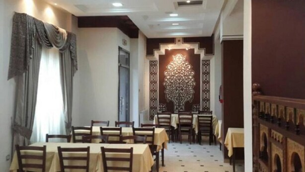 A dining area with tables and chairs, a decorative wall, and a patterned floor. - Hotel Roza (Algiers)