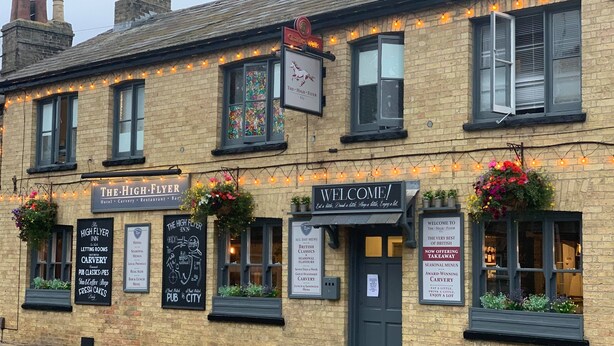 A building with multiple signs indicating it is The High Flyer Inn, offering services like hotel, carvery, restaurant, and bars. - The High Flyer (Ely)