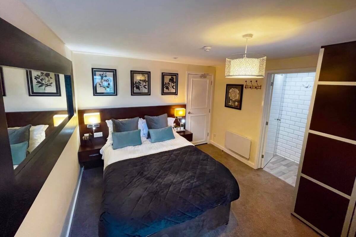 A hotel room with a large bed, bedside tables with lamps, a wardrobe, and framed pictures on the wall.