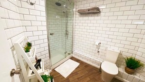 A bathroom with white subway tiles, a glass shower enclosure, a white toilet, and a wooden floor. - The High Flyer (Ely)