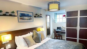 A hotel room with a bed, bedside lamps, a desk, a chair, a wardrobe, and a large window. - The High Flyer (Ely)