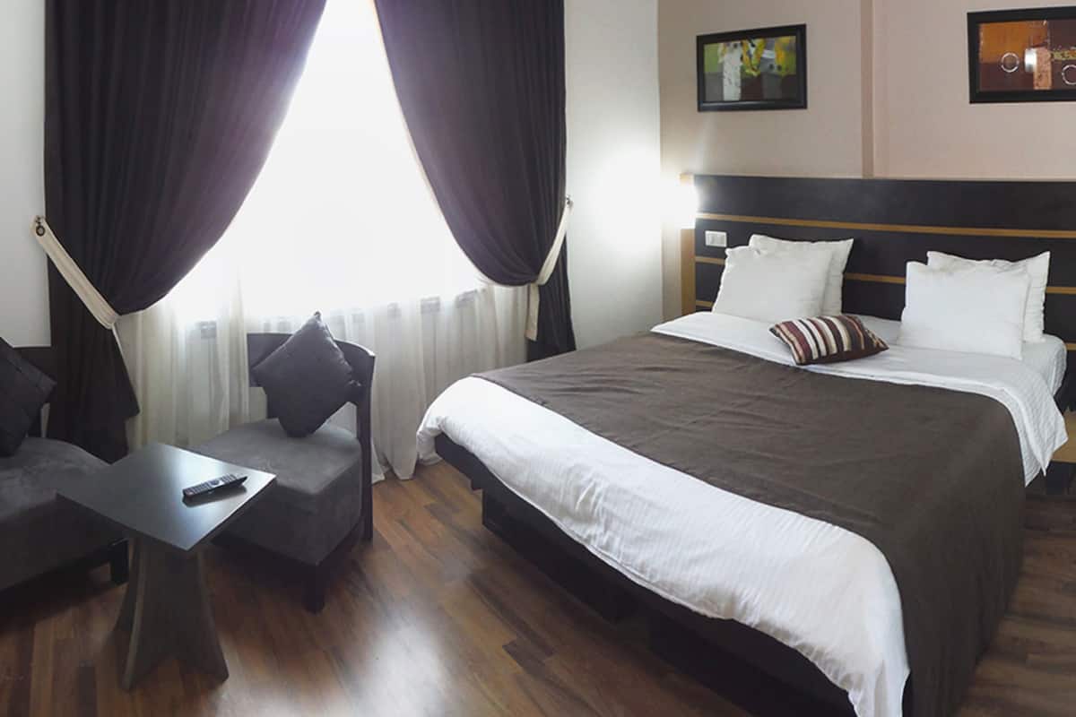 A hotel room with a large bed, a small sofa, a table, and a chair.