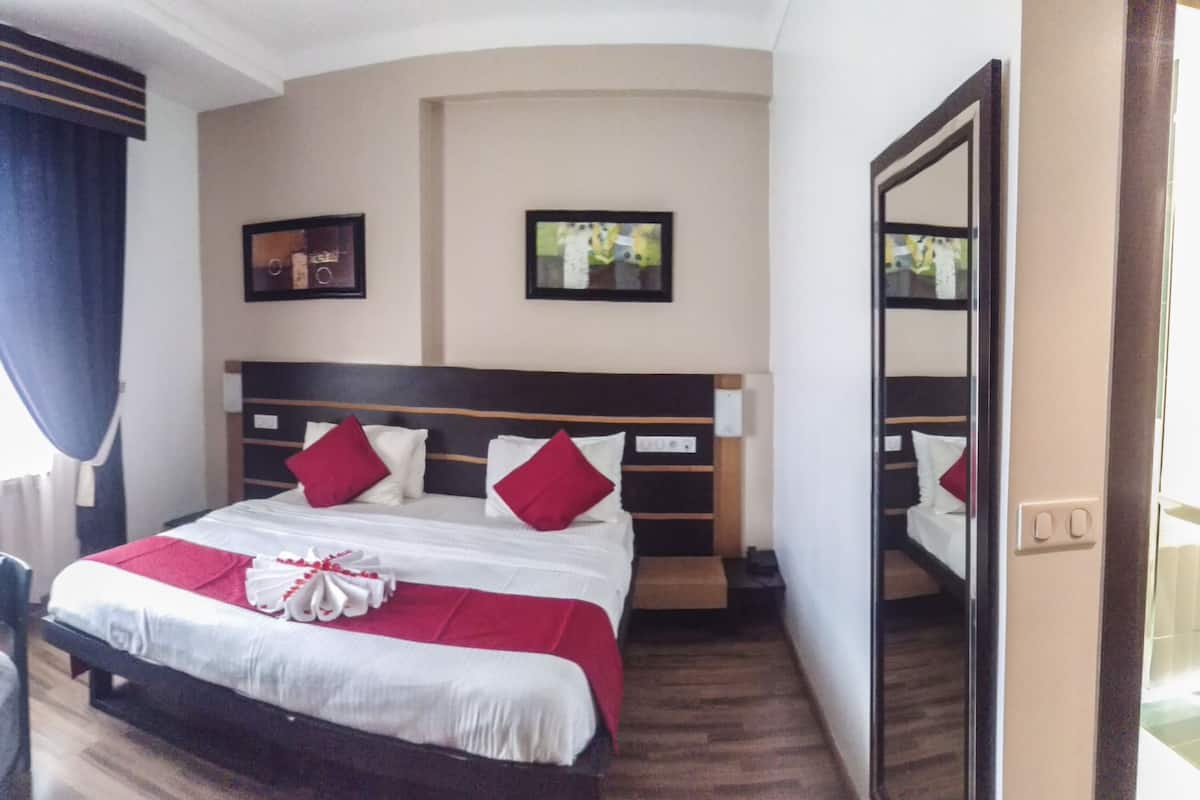 A hotel room with a bed, a desk, a chair, a window with curtains, and a nightstand.