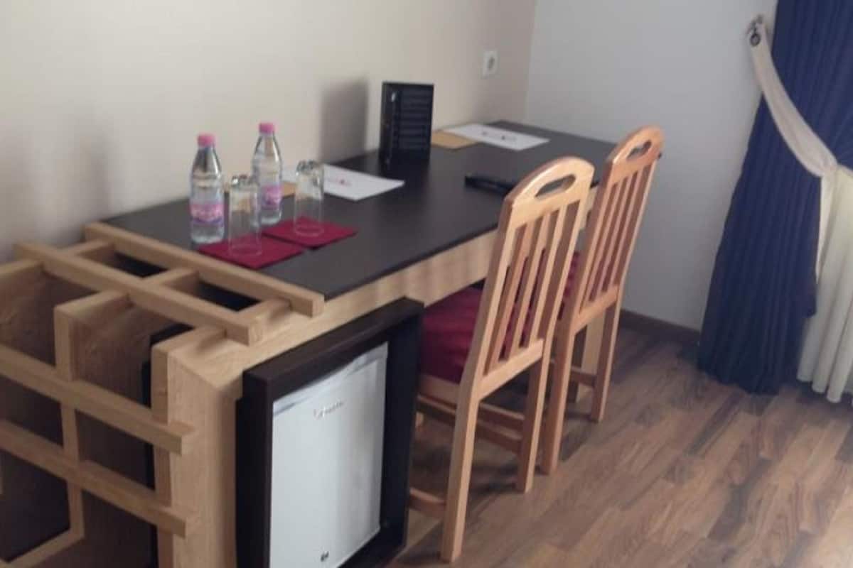 A compact room with a small refrigerator, a wooden table, two chairs, and a window with curtains.