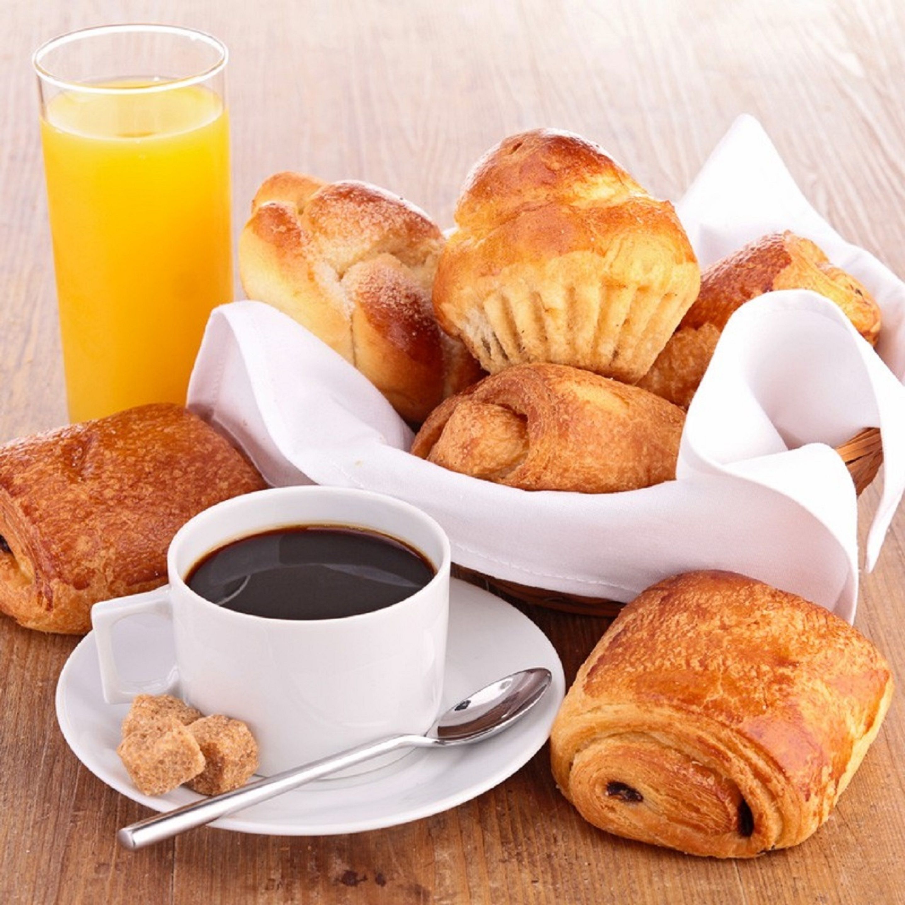 A breakfast setting with pastries, a cup of coffee, and a glass of orange juice on a wooden table.