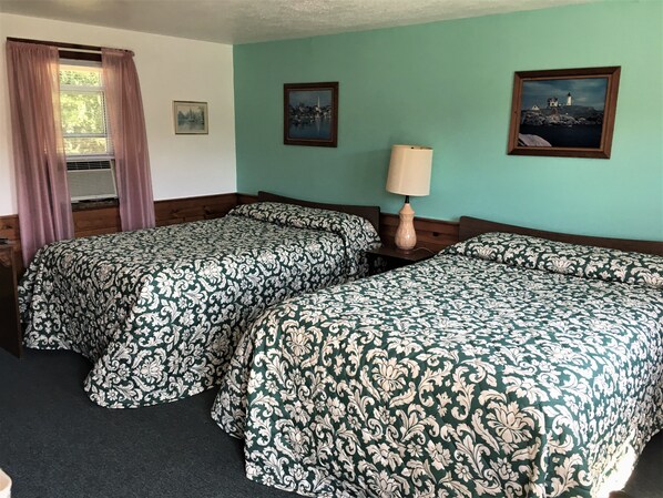 Una habitación con dos camas, una ventana con cortinas, una lámpara y dos cuadros en la pared.